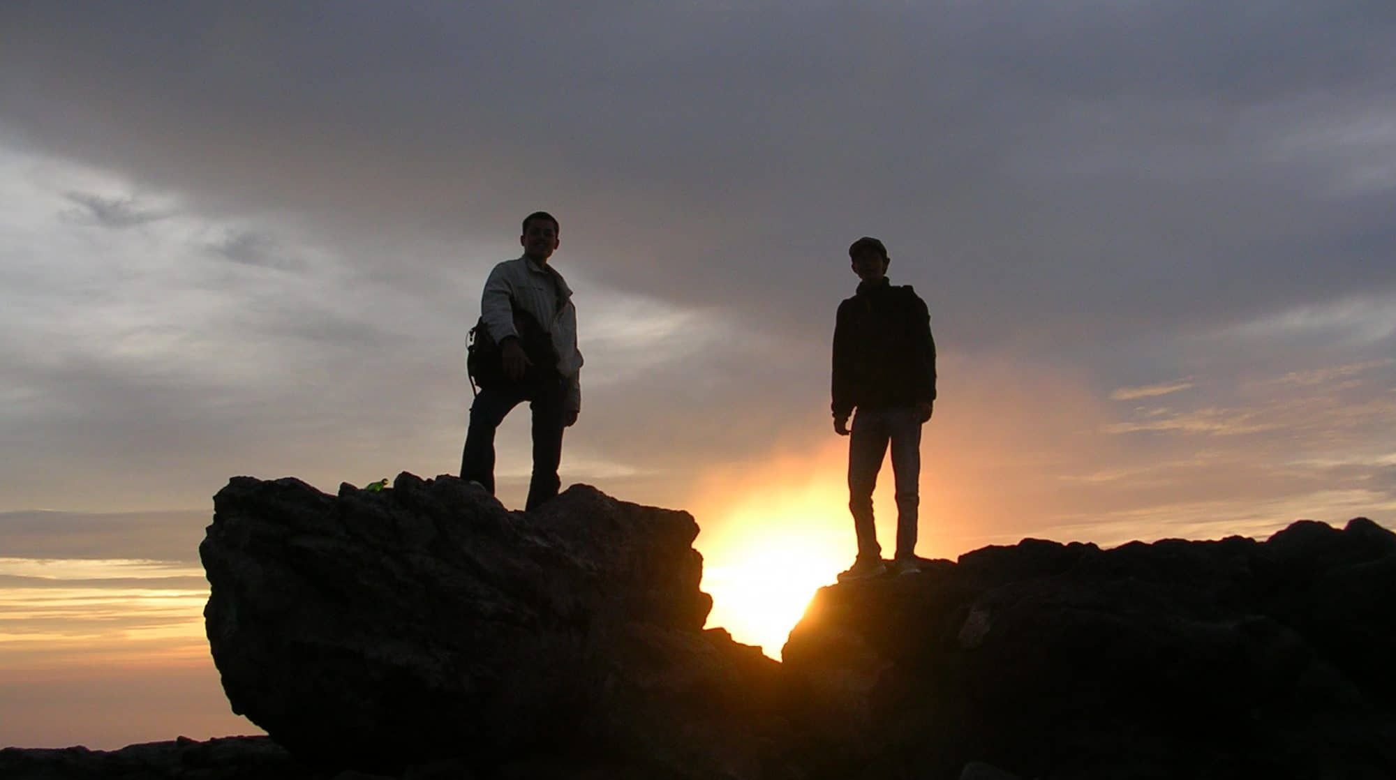Two silhouettes at sunrise on Merapi's volcanic rocks — the view many visitors come for