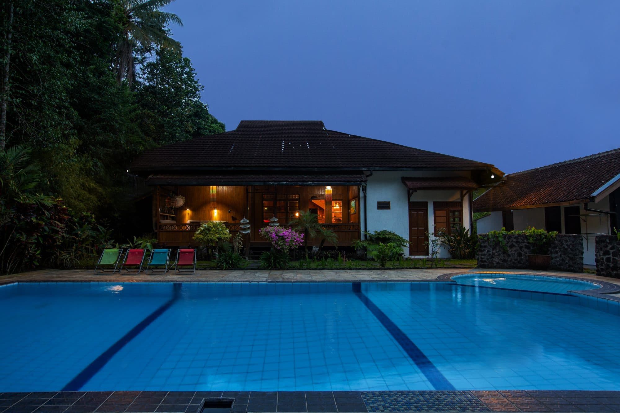 Villa Tanen at dusk: the private pool in the foreground, the lit wooden house behind, surrounded by tropical garden