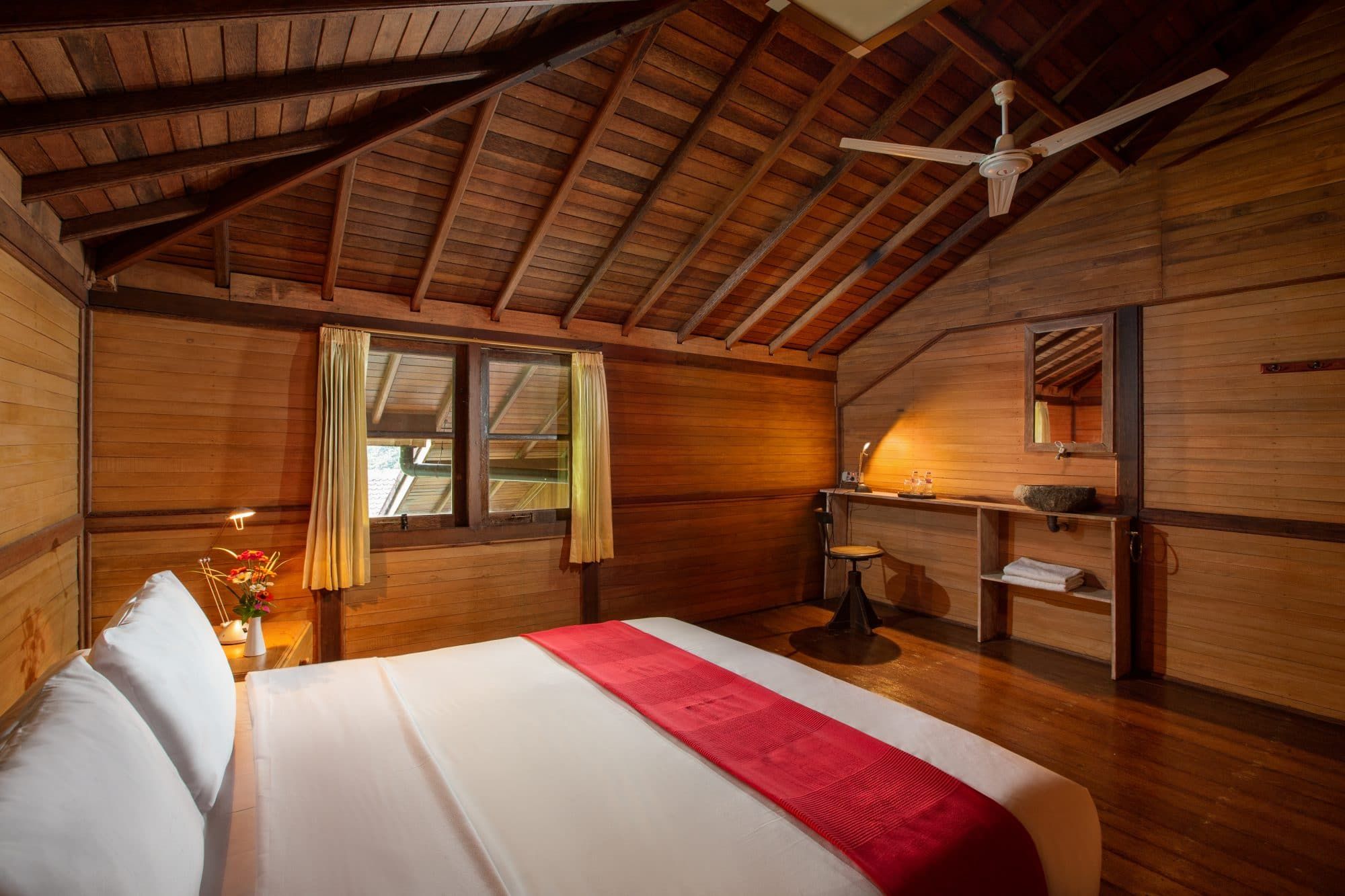 Bedroom at Villa Tanen with timber plank floor, double bed with red accent runner and ceiling fan