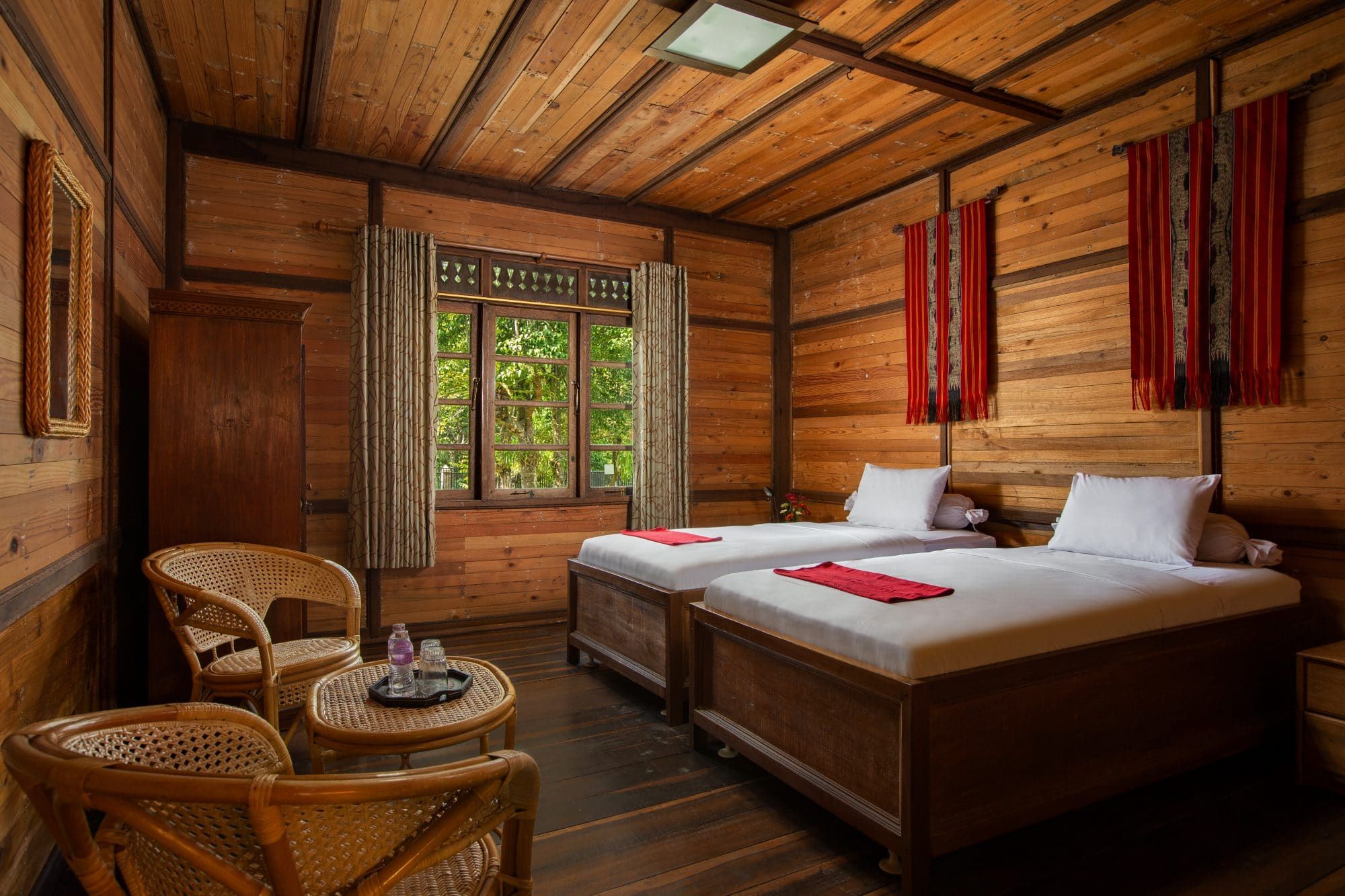 Twin-bed room at Villa Tanen with wooden walls, two single beds with red accents and rattan chairs by the window