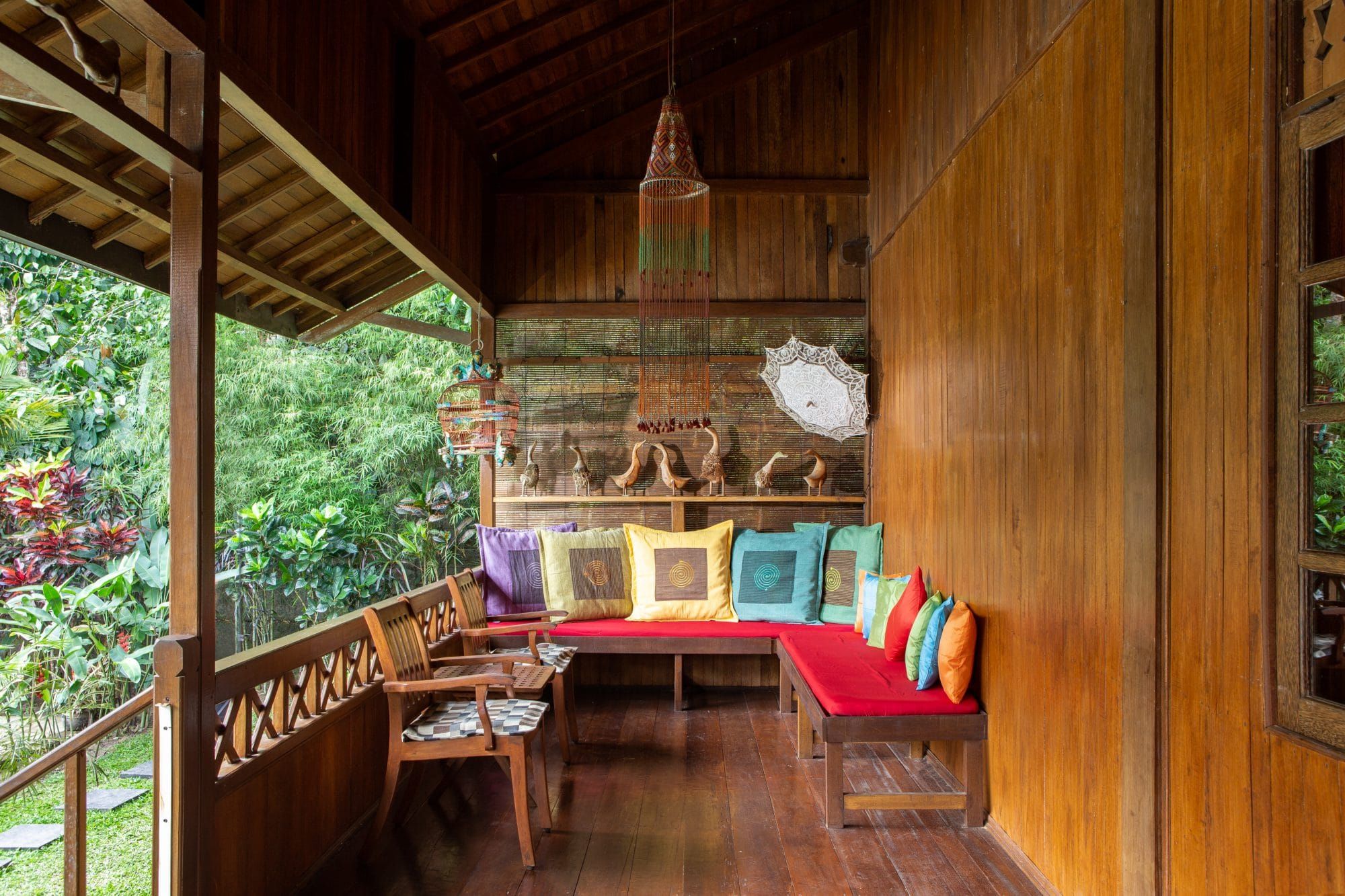 Warm wooden veranda of Villa Tanen with colourful cushions and a view into the tropical garden — the family's living room
