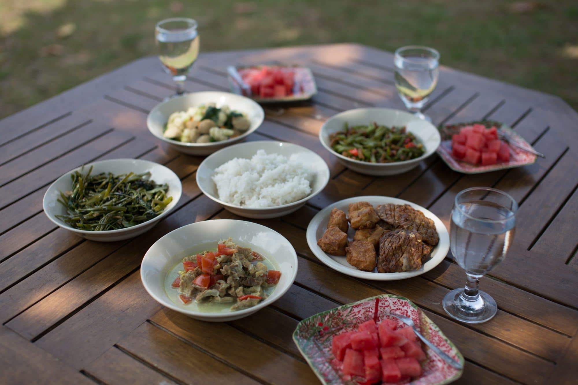 A generous Javanese meal on a wooden garden table at Villa Tanen — rice, vegetables, meat and fresh watermelon, prepared by the hostesses