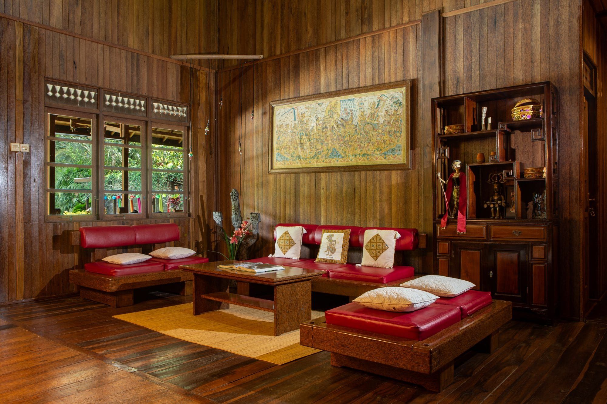Villa Tanen living room — dark teak wood, Javanese artwork on the wall, red leather seating